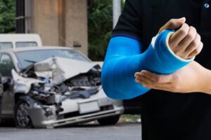 A man holding his fractured arm with crashed car in background