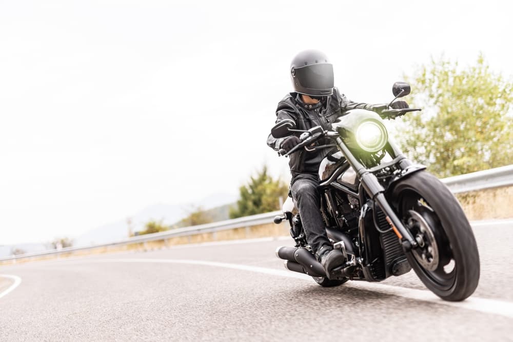 High key image of a man riding a chopper motorcycle on an open road, with clear skies and minimal shadows, showcasing the rider in motion.