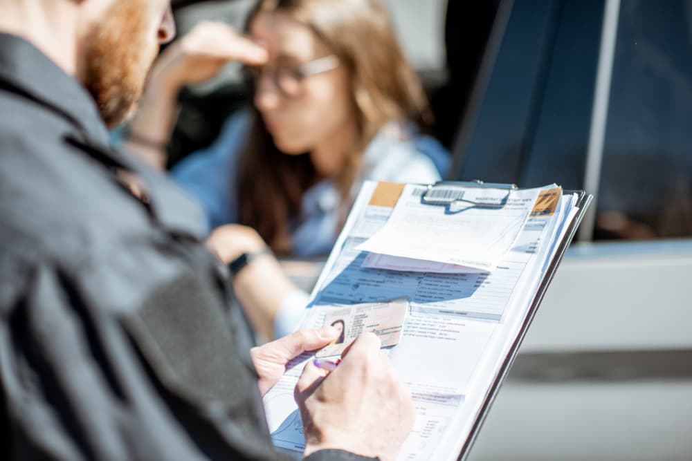 Policeman issuing a fine to a young woman driver for violating traffic rules, with a close-up view focused on the folder holding the fine.